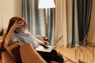 Evden çalışan serbest çalışan kadın, uzun saatler süren bilgi işleme ve uzak çoklu görev süreçlerinden kaynaklanan ekran anksiyetesi, bilişsel gerginliği ve dijital patlamayı gösteren jest olarak alnını tutuyor.