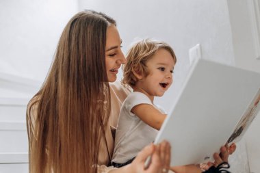 Neşeli bir anne, meraklı çocuğuyla birlikte bir kitap okuyor. Uluslararası Edebiyat Günü 'nü kutluyor ve sıcak, huzurlu bir evde erken yaşta hikaye anlatmayı ve sevgi dolu anları kucaklıyor. Anne ve onun mutlu anlarını.
