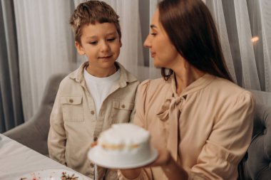 Anne ve oğlu, anne ve babasının duygusal sıcaklık ve sıcaklıkla dolu huzurlu bir aile kutlaması sırasında birbirlerine sevgi dolu bakışlar atarken beyaz buzlu bir pasta sunarken sakin ve samimi bir anı paylaşıyorlar.