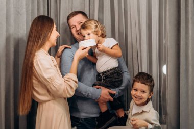 Gerçek aile anı duygusal bir bağ kuruyor. Anne, bebeğe pasta tutarken, baba onu destekliyor ve büyük kardeş gülüyor. Kutlama sırasında sıcak, neşeli bir ortam yaratıyor.