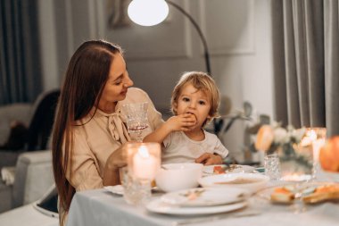 Huzurlu bir doğum günü anı. Anne, çocuğuna sevgi dolu bir şekilde mum ışığı ve çiçeklerle sarılıyor. Sıcak ve sessiz bir evde duygusal bağlılık ve şefkat dolu bir kutlama yapıyor.