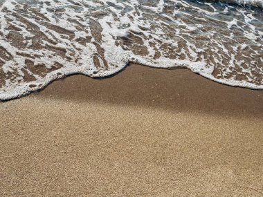 Sahilde hafif dalgaların dalgalandığı sakin bir sahil sahnesi. Su tarafından oluşturulan ince kum ve ince desenlerle. Sakin okyanus huzurlu bir atmosferi yansıtır. Kumsalın yakın görüntüsü.