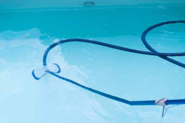 Rutin bakım sırasında özel bir yüzme havuzunun sualtı görüntüsü berrak suyun altında görünen mavi bir vakum hortumu mevsimlik havuz temizleme rutinini güncel hava koşullarında vurguluyor.