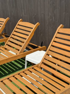 Yaz güneşinde suni çimenlerin üzerindeki ahşap şezlonglar gölgelerle güçlendirilmiş temiz, modern bir açık hava ortamı yaratır ve en az beyaz masa yaşam tarzı teması ve mimari arka plan için mükemmeldir.