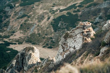 Dağların yamacındaki kaya oluşumu yumuşak sonbahar güneşi engebeli dokuları vurgular ve dingin dağlık arazideki uzak tepeleri sıcak toprak tonlarıyla sonbaharın başlarında doğal vahşi atmosferi vurgular.