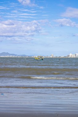 Güneşli bir günde sakin mavi sular, demirli tekneler ve doğal kaya oluşumlarıyla çekilen huzurlu bir plaj sahnesi. Güneş ışığı kıyı şeridinin güzelliğini arttırır. Mükemmel bir huzur anı sunar ve deniz kıyısından kaçar..