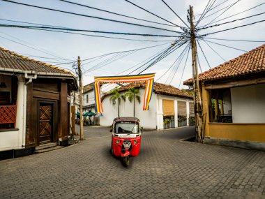 Üç Tekerlekli, Sonsuz Hikayeler. Kırmızı bir tuktuk Galle, Sri Lanka 'nın kaotik sokaklarında ilerliyor.