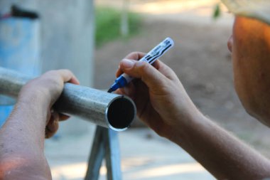 Silindirik metal bir tüpün etrafına çizgi çekmek için mavi işaret kullanan ellerin yakınlaştırılması