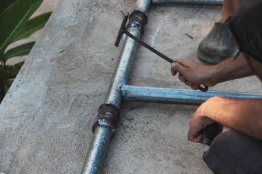 Bir insan metal borulardaki bir kaynak yerinden kir çıkarmak için bir alet kullanıyor, muhtemelen bir çekiç.