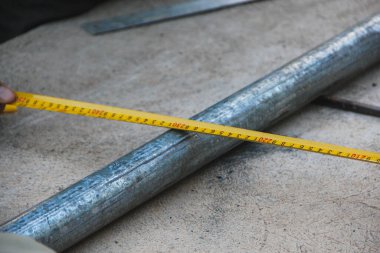 Bir el silindirik metal bir tüpe karşı sarı şerit ölçü tutar, bu da santimetre cinsinden bir ölçü gösterir.
