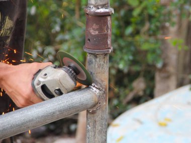 Metal borular üzerinde çalışmak için bir açı öğütücü kullanarak ellerinizi kapatın, kıvılcımlar saçın.