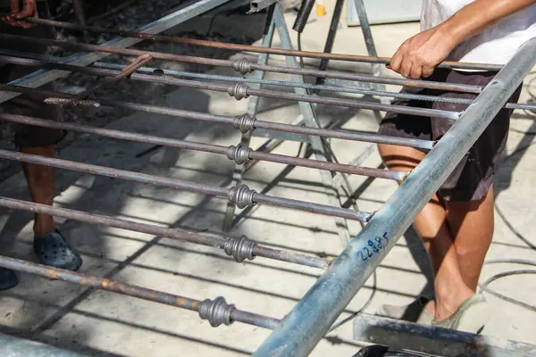 Metal bir çerçeve üzerinde kaynak yapmaya hazır gibi görünen iki kişi metal çubukları bir arada tutuyor.