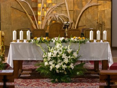 Beyaz bir bez, uzun mumlar ve kutsal bir tören için hazır taze beyaz ve sarı çiçeklerle süslenmiş bir kilise sunağının saygıdeğer manzarası.
