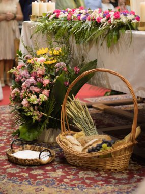 Ekmek, üzüm ve buğdayla örülmüş bir sepetin, canlı çiçeklerle birlikte kutsal bir tören için hazırlandığı kilise sunağının geniş bir görüntüsü.