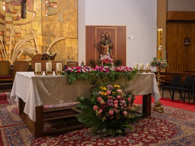 Dini bir tören için çok güzel dekore edilmiş bir kilise sunağı, canlı çiçek aranjmanları, uzun mumlar, ve bir heykel, şenlikli kutsal bir yer yaratıyor.