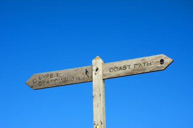 Mavi gökyüzü, West Bay, Dorset, İngiltere ve Avrupa 'ya karşı Eype ve Seaton' a yürüyüş güzergahı olan tahta sahil yolu işareti.