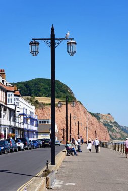 SIDMOUTH, İngiltere - 11 Ağustos 2022 - Solda oteller bulunan gezinti güvertesinde dinlenen turistler Pennington Point, Sidmouth, Devon, İngiltere, Avrupa, 11 Ağustos 2022.