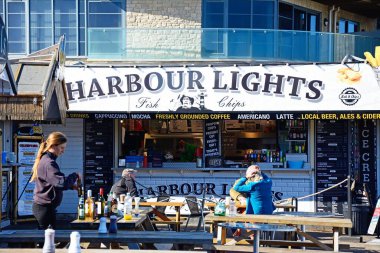 BATI BAY, İngiltere - 10 Ekim 2022 - Liman Bölgesi, Batı Körfezi, Dorset, İngiltere, Avrupa, 10 Ekim 2022 'deki Harbour Lights kafe restoranının önünde oturan turistler.