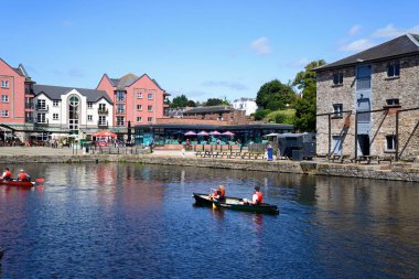 EXETER, UK - 22 AĞUSTOS 2023 - 22 Ağustos 2023 'te Exeter kanalı üzerinde kano süren insanlar Piazza Terracina' da kafeler ve restoranlar ile arkada, Exeter, Devon, 22 Ağustos 2023.