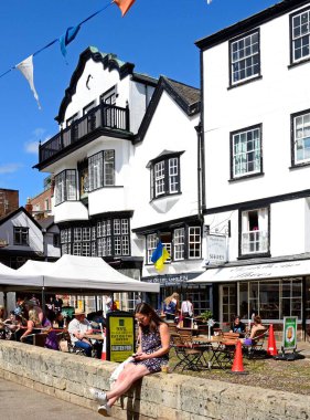 EXETER, UK - 22 AĞUSTOS 2023 - Katedralin önünde bir kaldırım kafesi olan Mols Close 'un önü ve duvarda oturan ve telefonuna bakan bir kadın, Exeter, Devon, İngiltere, Avrupa, 22 Ağustos 2023.