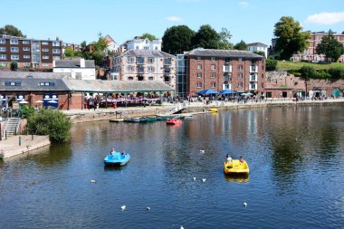 EXETER, UK - 22 AĞUSTOS 2023 - Doğu Rıhtımı boyunca mağazaları ve restoranları bulunan River Exe üzerinde pedallar üzerinde turistler, Exeter, Devon, UK, Europe, 22 Ağustos 2023.