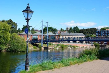 EXETER, UK - AUGUST 22, 2023 - View of the Cricklepit suspension bridge over the River Exe with a traditional street light in the foreground and quayside restaurant to the rear, Exeter, Devon, UK, Europe, August 22, 2023. clipart