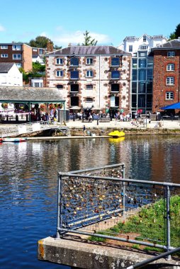 EXETER, UK - 22 AĞUSTOS 2023 - Exe Nehri 'nin karşısındaki East Quay boyunca uzanan dükkanlara ve restoranlara doğru ön plandaki Exeter, Devon, İngiltere, Avrupa, 22 Ağustos 2023.