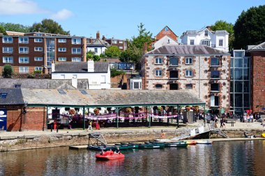 EXETER, UK - 22 AĞUSTOS 2023 - Doğu Rıhtımı boyunca mağazaları ve restoranları bulunan River Exe üzerinde pedallara binen turistler, Exeter, Devon, İngiltere, Avrupa, 22 Ağustos 2023.