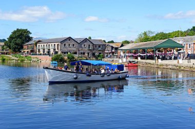 EXETER, UK - 22 AĞUSTOS 2023 - Doğu Şeria Quay restoranları ve dükkanları ile Exeter Nehri üzerinde bir tur teknesine binen yolcular, 22 Ağustos 2023.
