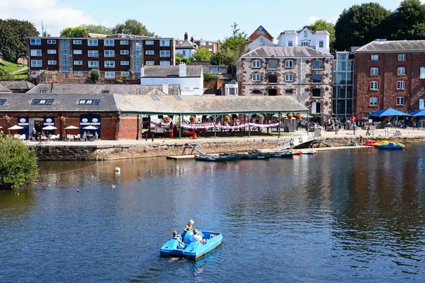 EXETER, UK - 22 AĞUSTOS 2023 - Doğu Rıhtımı boyunca mağazaları ve restoranları bulunan River Exe üzerinde pedallı turistler, Exeter, Devon, UK, Europe, 22 Ağustos 2023.