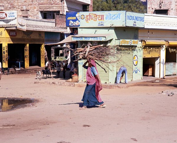 INDIA, JAIPUR - NOVEMBER 22, 1993 - Indian woman walking along a village street carrying firewood on her head, Jaipura, Rajasthan, India, November 22, 1993.
