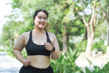 Asyalı ve cüsseli bir kadın yaz parkında dışarıda egzersiz yapıyor.