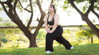 Güneşli bir yaz gününde doğada yoga yapan güzel ve iri bir kız. Atletik giyimli bir kadının portresi doğal ortamdaki spor ve refah ortamında bir hamleyi gerçekleştirir. Asyalı artı beden kadın.