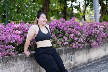 Asyalı ve cüsseli bir kadın yaz parkında dışarıda egzersiz yapıyor.