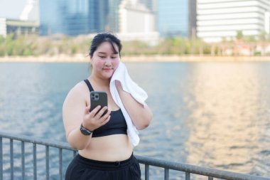 Gençlerin portresi, arka planda belediye binaları olan bir su kütlesinin yanında telefonlarını kontrol ederken alnından teri siliyor. Asyalı artı beden kadın.