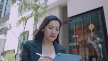 Şehir caddesinde yürürken stil ve tablet kullanan çekici bir iş kadını. 