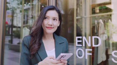 Şehir caddesinde cep telefonu kullanan takım elbiseli çekici Asyalı iş kadını. 