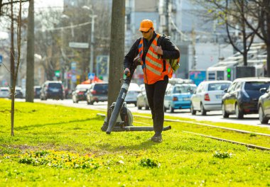 Şehir parkında ağır yaprak üfleyicisi çalıştıran bir işçi. Sonbaharda düşen yaprakları toplamak. Park temizleme servisi