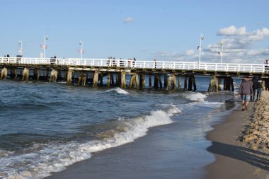 Bir adam güneşli bir günde eski bir limanda yürüyor.