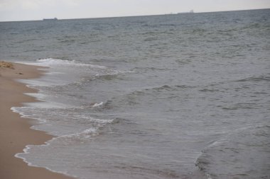 Fotoğraf kumlu bir kıyıya vuran deniz dalgalarını gösteriyor. Dalgalar ve kumla doğal kıyı manzarası