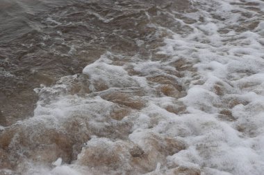 Fotoğraf kumlu bir kıyıya vuran deniz dalgalarını gösteriyor. Dalgalar ve kumla doğal kıyı manzarası