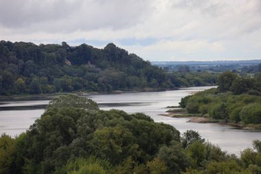 Yeşil tepeler ve yoğun bitki örtüsünden akan Vistula Nehri 'nin havadan görünüşü. Sahne güneş ışığıyla aydınlatılır gökyüzünde bulutlar ışık ve gölgenin karşıtlığını yaratır..