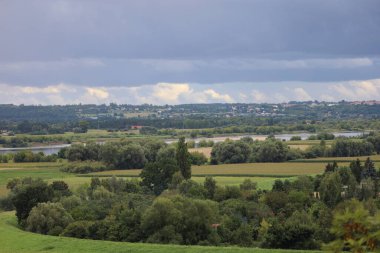 Polonya 'nın Swiecie kenti yakınlarındaki Vistula Nehri' nin manzarası, yeşil ve doğal manzarayla çevrili, ufukta görünen küçük binalar parlak bir gökyüzünün altında..