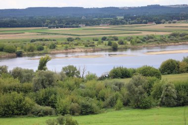 Polonya 'nın Swiecie kenti yakınlarındaki Vistula Nehri' nin manzarası, yeşil ve doğal manzarayla çevrili, ufukta görünen küçük binalar parlak bir gökyüzünün altında..