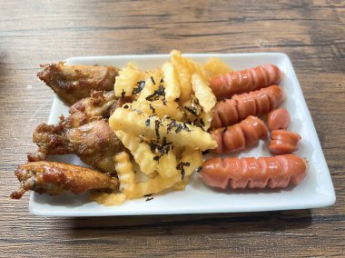 Tavuk, patates kızartması, sosis ve ahşap bir masada nefis kızarmış yemek tabağı..