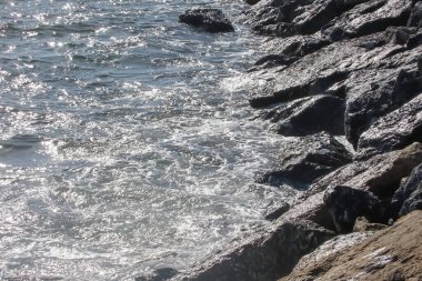 Renkli bir sonbahar gününde hafif rüzgarın esintisiyle canlanan güneş gökyüzünde parlıyor ve denizin dalgalı yüzeyi büyüleyici bir manzara sunuyor. Sakin bir sonbahar gününde dalgalı deniz manzarası. Dalgalı Deniz Burnu Güneşli Gökyüzünün Altında .