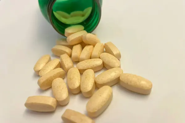 Vitamin pills spilling out of a green bottle on white background.medicine pills in green bottle on white background, close up. Macro photo.Pills spilling out of pill bottle on white background.