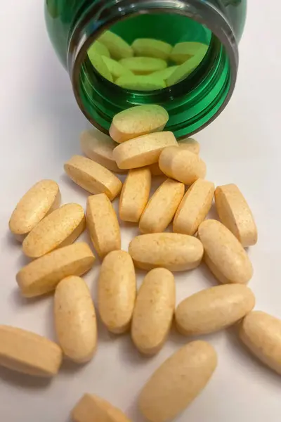 Vitamin pills spilling out of a green bottle on white background.medicine pills in green bottle on white background, close up. Macro photo.Pills spilling out of pill bottle on white background.
