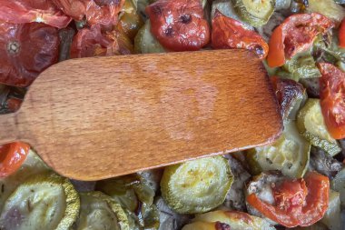 Pişirme tepsisinde sebzeler. Tahta spatula. Domates, biber, patlıcan ve kabak servis etmeye ve yemeye hazır. Fırında kaynıyor..