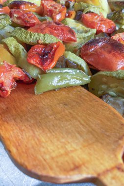 Pişirme tepsisinde sebzeler. Tahta spatula. Domates, biber, patlıcan ve kabak servis etmeye ve yemeye hazır. Fırında kaynıyor..